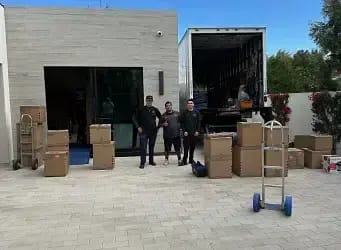 SD Moving Services crew standing outside a residence with stacked moving boxes and a loaded transport truck.