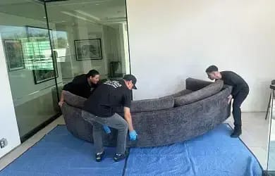 SD Moving Services team carefully lifting and positioning a large curved sectional sofa onto protective moving pads inside a home.