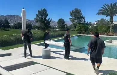 Moving crew setting up patio umbrellas and outdoor furniture around a pool at a Palm Desert estate.