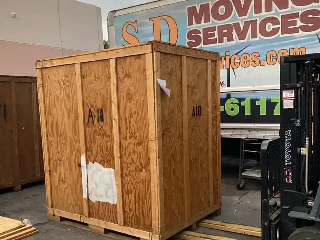 Large wooden storage crate being loaded by a forklift outside the SD Moving Services facility in Palm Desert near Palm Desert